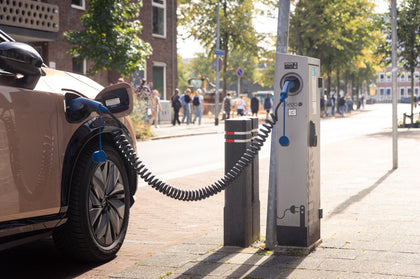 Electric car charging at a street-side charging station with people in the background.