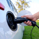 Hand plugging the Type 1 connector into the charging port of a white electric car